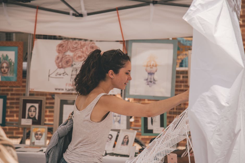 A young woman browsing art prints at an outdoor market stall.